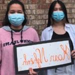 Two students in masks hold a sign that says welcome in vietnamese